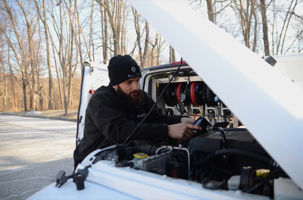 Slick W-2 technician performing maintenance under a vehicle hood